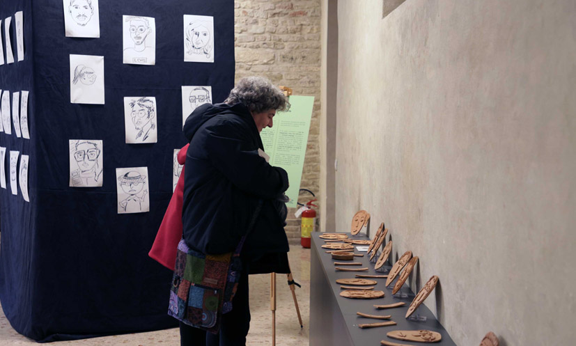 Il pannello della mostra con le caricature dei volti e alcuni lavori in ceramica.